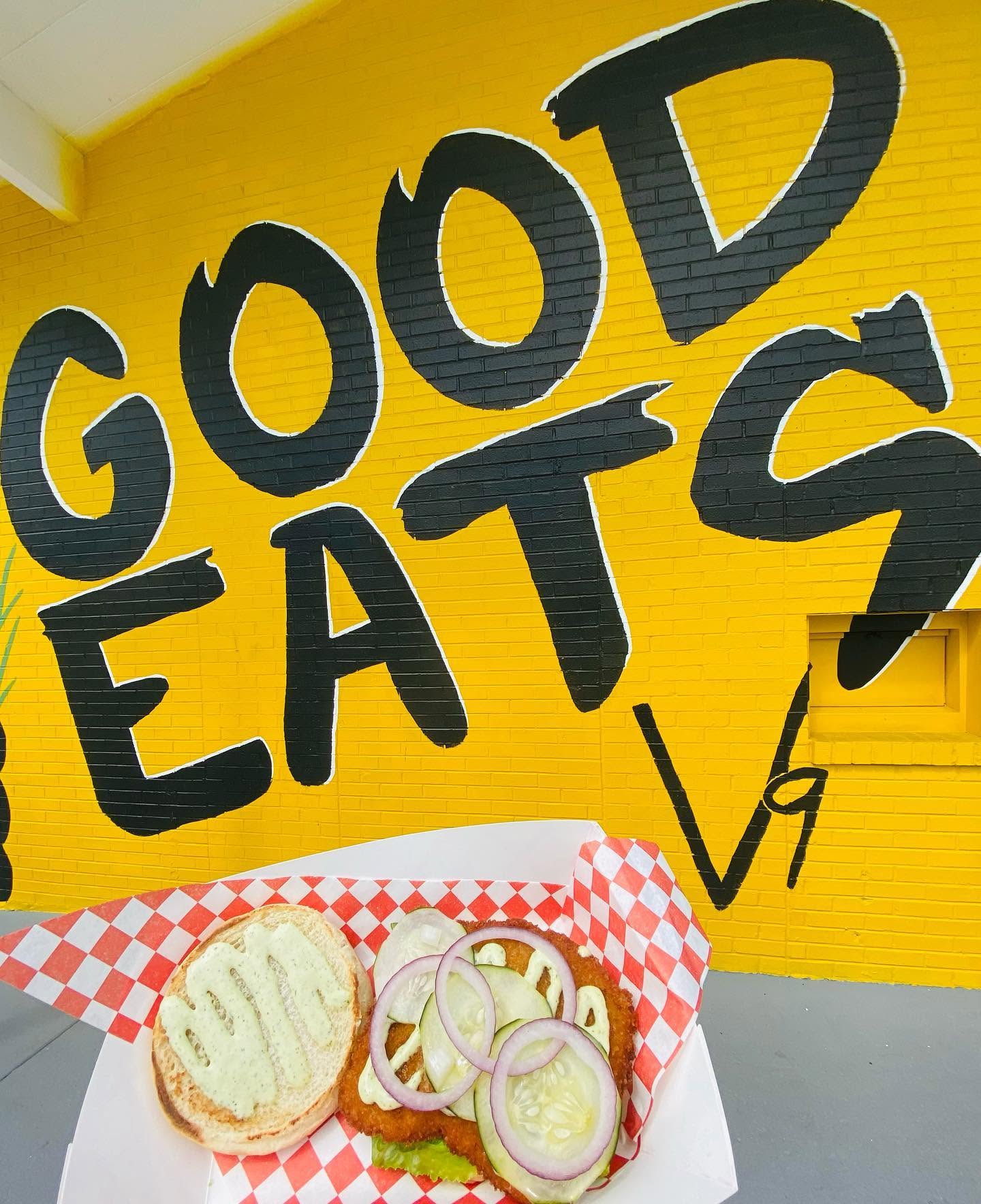 The hand-painted GOOD EATS wall at V9 EATS in sunflower yellow, a sandwich basket on red-and-white checker paper in front