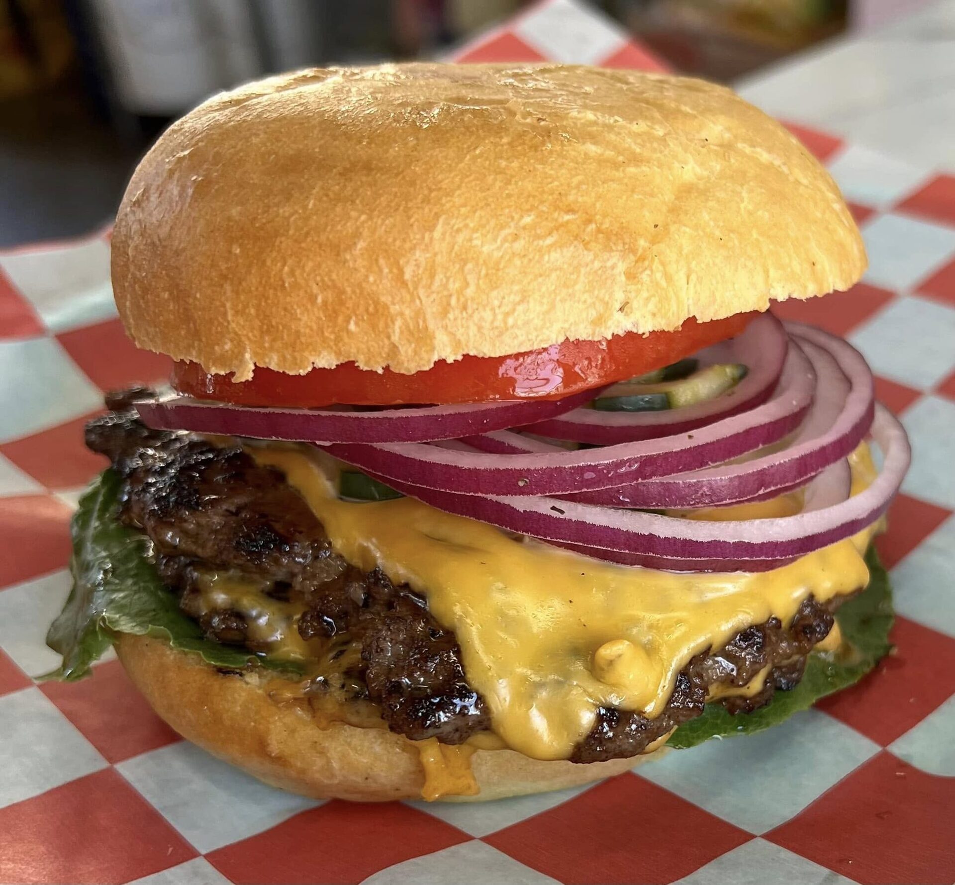 Double smash cheeseburger with tomato and red onion on checker paper