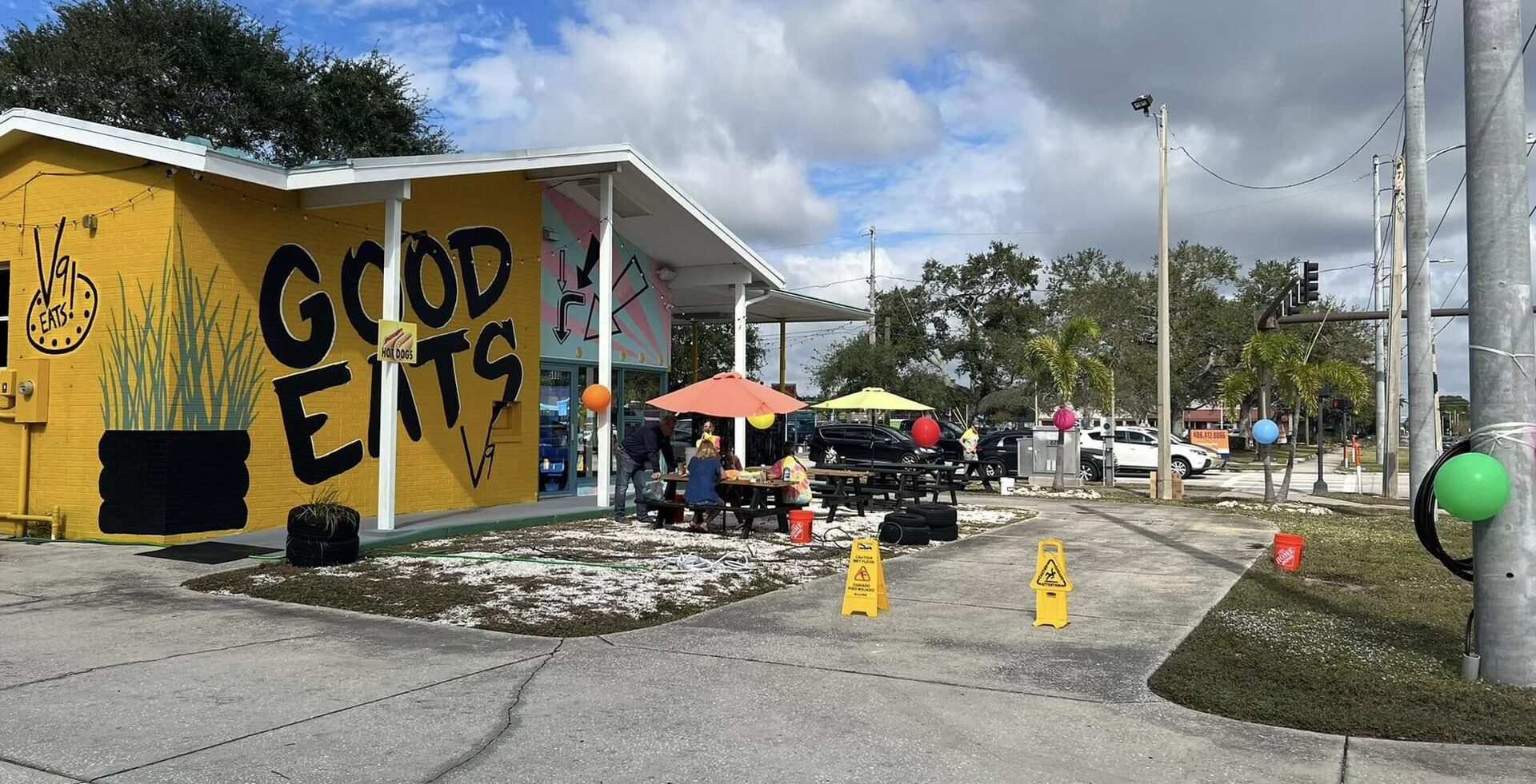 V9 EATS from the parking lot: the yellow GOOD EATS wall, the canopy and patio umbrellas on 9th Ave N