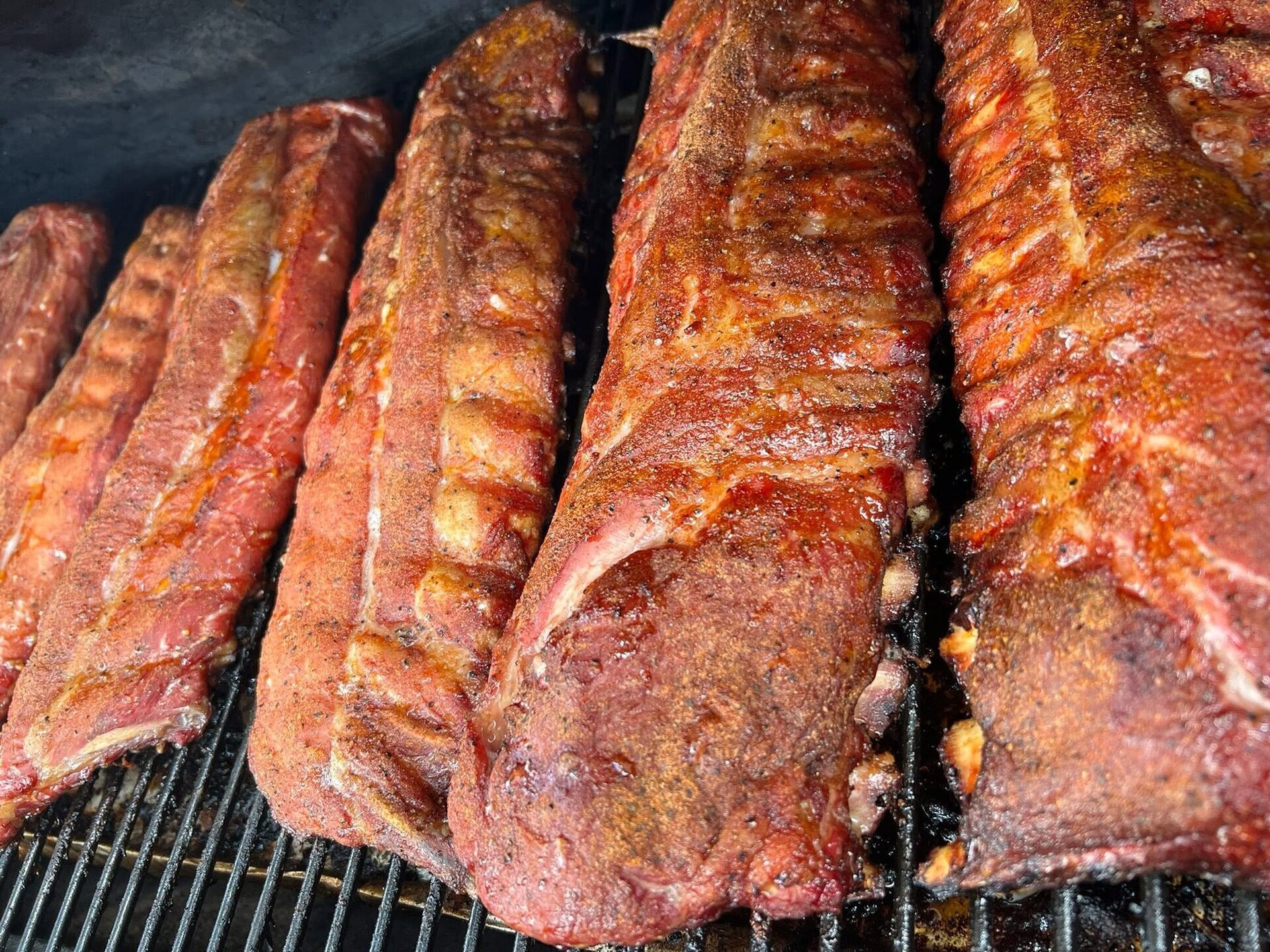Racks of baby back ribs smoking on the grate of V9's smoker out front