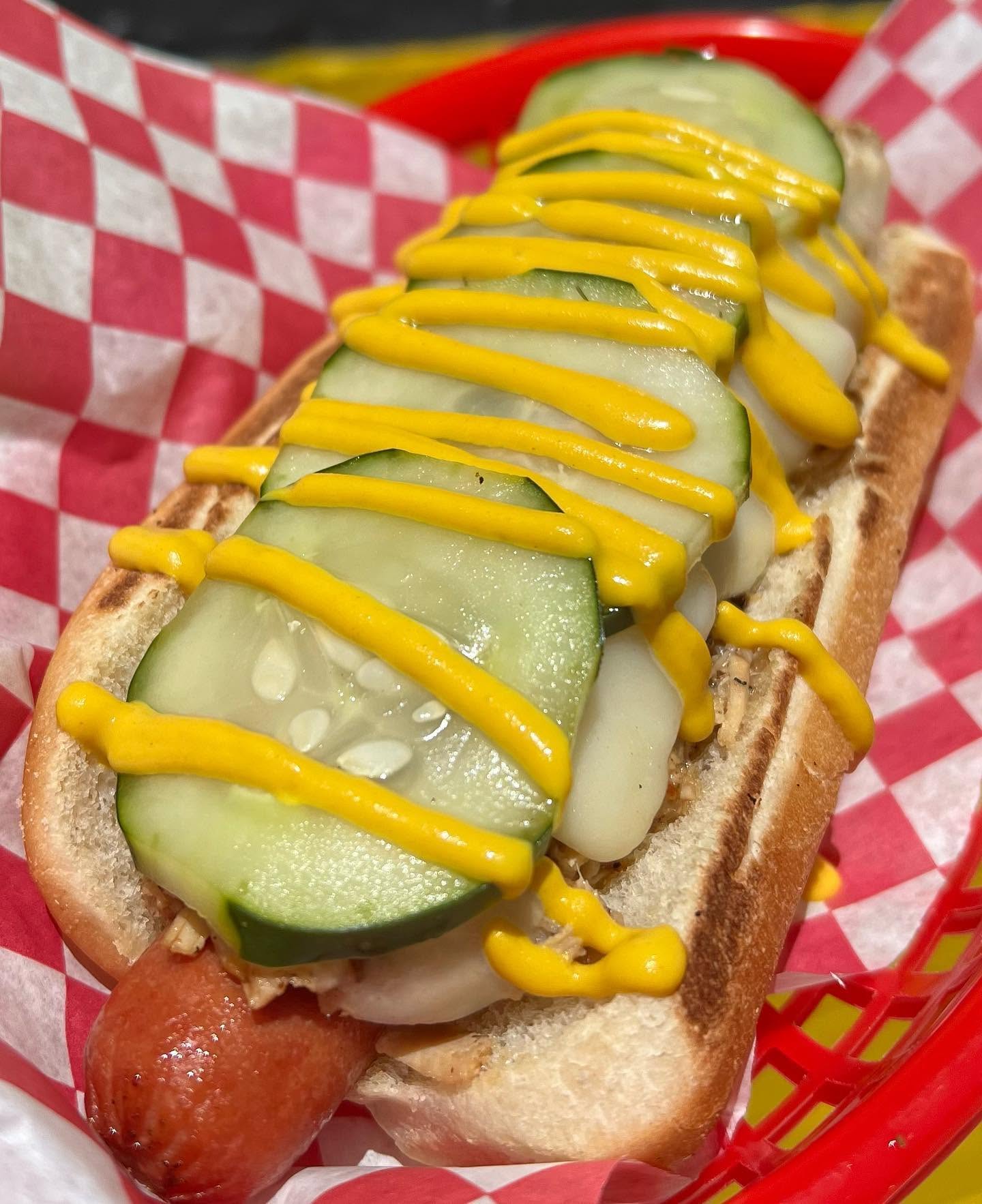 Hot dog with pickle spears, onions and yellow mustard in a checker-lined basket