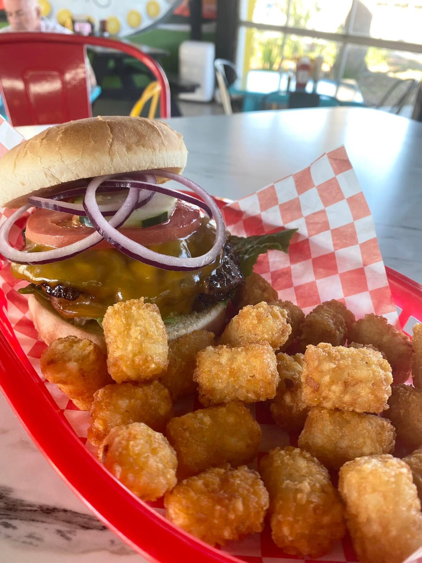 Burger with a heap of tater tots in a red basket