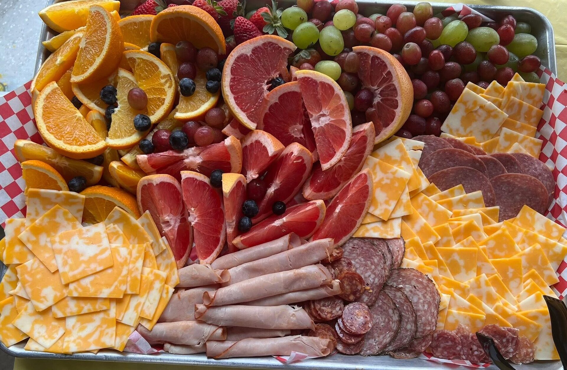 An overhead party tray of citrus, grapes, cheese and sliced meats